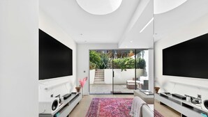 Een moderne woonkamer met een flatscreen televisie, een groot vloerkleed en een schuifdeur die uitkomt op een terras.
