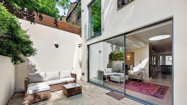 Een moderne patio met rieten meubilair, een glazen deur naar een interieur met een bank en een eethoek.