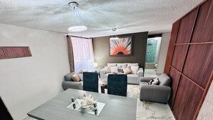 A modern living room with a dining area, grey sofas, a dark upholstered chair, and a large abstract painting on the wall. - Medellín 210  (Ciudad de México)