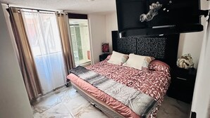 A bedroom with a bed, a headboard, a nightstand, a window with curtains, and a view of a balcony. - Medellín 210  (Ciudad de México)