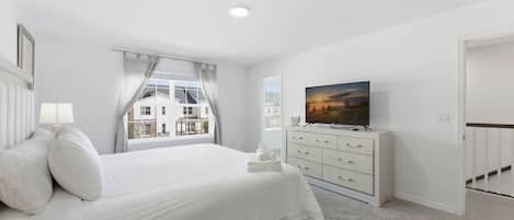 Un dormitorio con cama, cómoda, televisor y ventana con cortinas.
