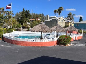 En swimmingpool i tropisk miljø med stråtag parasoller og liggestole.