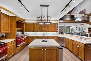 A spacious kitchen with wooden cabinetry, a central island, and a staircase leading to an upper level. - Lily Pad Lake House @ Lake Fork (Yantis)