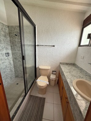 Een badkamer met een glazen douchecabine, toilet, toiletbrons en bad.