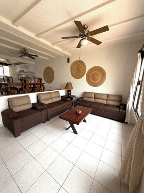 Ein Wohnzimmer mit einer Eckcouch, einem Couchtisch, einem Deckenventilator und einem Essbereich im Hintergrund.