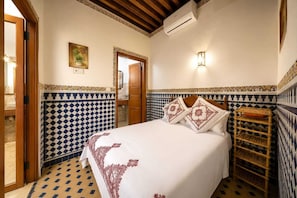 A bedroom with a bed, patterned walls, a wooden door, and a wall-mounted air conditioning unit. - Riad AL HANA (Fes)
