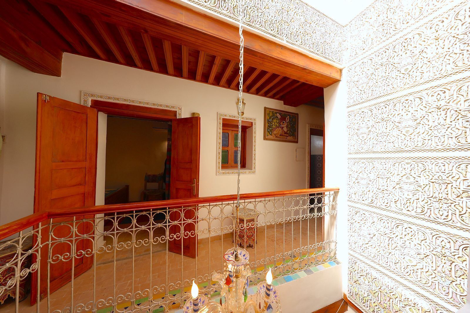 Un balcon doté d’une balustrade en fer forgé, de portes en bois et d’un luminaire suspendu.