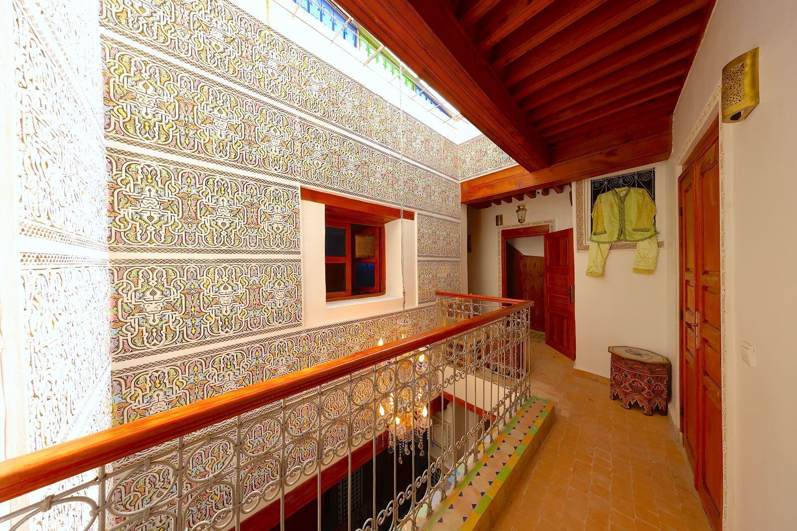 Un couloir orné de motifs complexes en mosaïque, une rambarde en bois et une petite fenêtre.