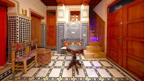 Um interior tradicional marroquino com soalho em azulejos, mobiliário de madeira e portas ornamentadas.