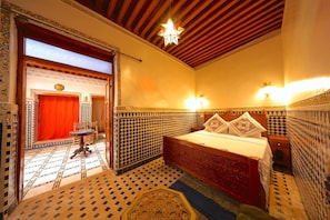 A room with a bed, a small table, and a decorative rug. - Riad AL HANA (Fes)