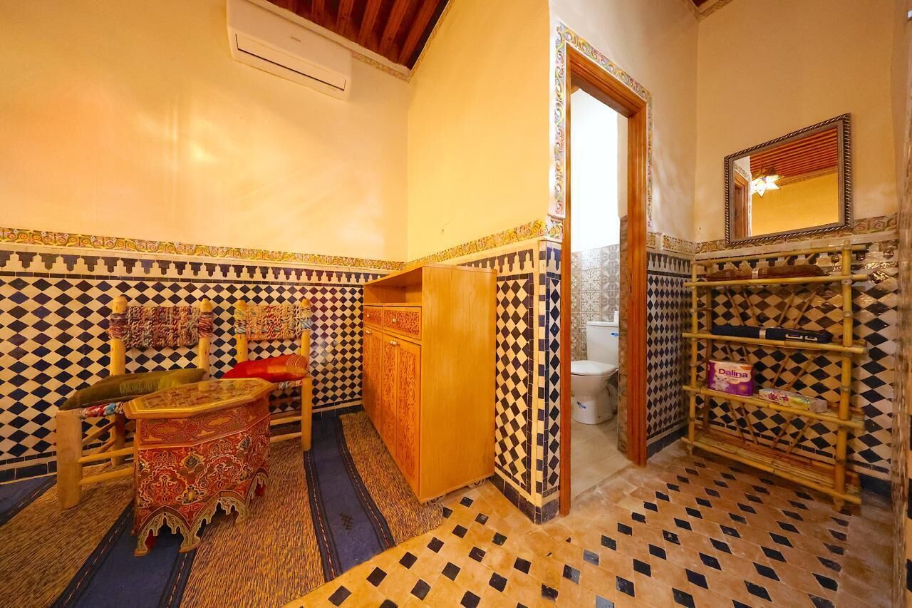A bathroom with patterned tiles, a wooden cabinet, a shelf with toiletries, and a mirror.