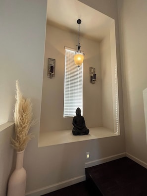 Une salle de méditation avec une statue, une fenêtre avec des stores et un luminaire suspendu.