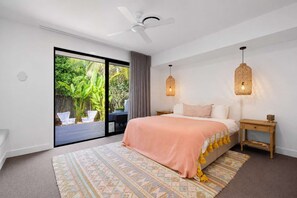 A bedroom with a bed, a ceiling fan, a nightstand, a lamp, and a view of greenery outside. - The Beachside House with Pool & Walk to Beach (Burleigh Heads)