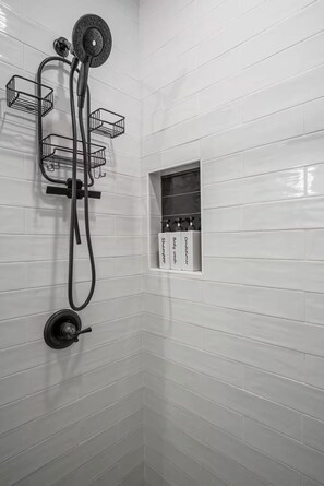 Eine Dusche mit Handbrause, Wandarmatur und Bedienknauf. An der Wand befinden sich drei schwarze Drahtkörbe.