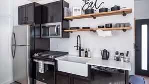 A modern kitchen with black cabinets, a stainless steel refrigerator, a microwave, a stove, a dishwasher, and wooden shelves with kitchenware. - Old Town Cottonwood-Walk to Shops & Dining (Cottonwood)