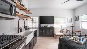 A modern kitchen with a built-in stove, microwave, and a coffee machine. There is a dining area with a table and chairs, and a black sofa. - Old Town Cottonwood-Walk to Shops & Dining (Cottonwood)