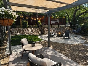 Ein überdachter Patio-Bereich mit Gartenmöbeln, einem Feuerkorb und einem hängenden Blumenkorb.