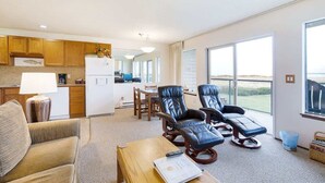 A spacious living area with a sofa, two reclining chairs, a wooden coffee table, and a kitchen in the background. - Hi-Tide Resort, Queen Bed, Dogs OK, Unit 7 (Moclips)