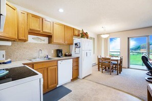 A kitchen with wooden cabinets, a dishwasher, a refrigerator, a dining area with a table and chairs, and a view of the outdoors.