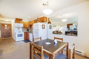 Cocina compacta con mesa de comedor, armarios de madera y refrigerador.