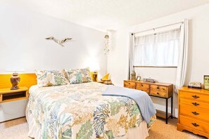 Un dormitorio con cama, mesitas de noche, cómoda, ventana con cortinas y decoración en las paredes.