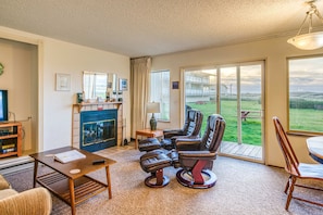 A living room with a fireplace, a television, a dining table, and a view of the outdoors.