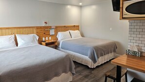 A hotel room with two beds, a wooden headboard, a small table, a TV mounted on the wall, and a brick-patterned wall. - Quest Motel (Whitewood)