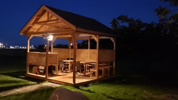 A wooden gazebo with a 'WELCOME' sign, outdoor seating, and a pathway leading to it. - Quest Motel (Whitewood)