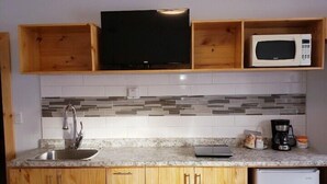 A compact kitchen with wooden cabinets, a microwave, a sink, and a coffee maker. - Quest Motel (Whitewood)