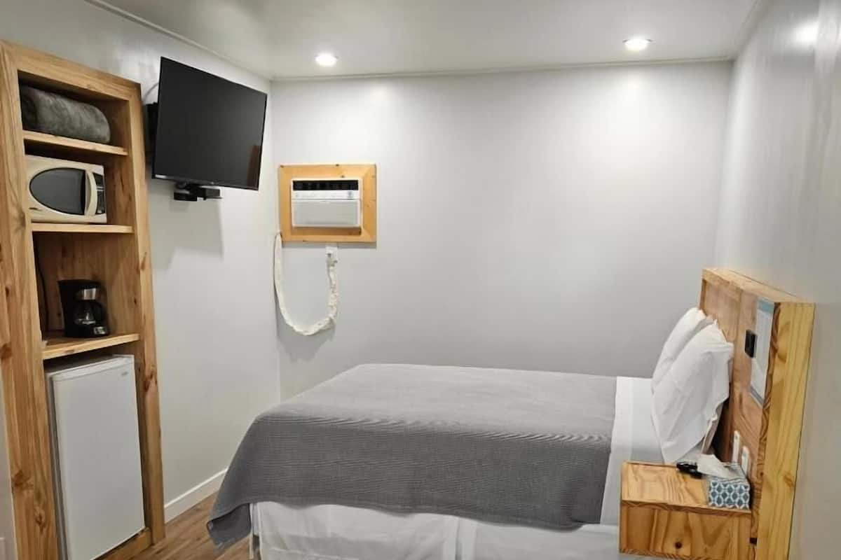 A bedroom with a bed, a TV, a mini-fridge, and a wooden shelf.
