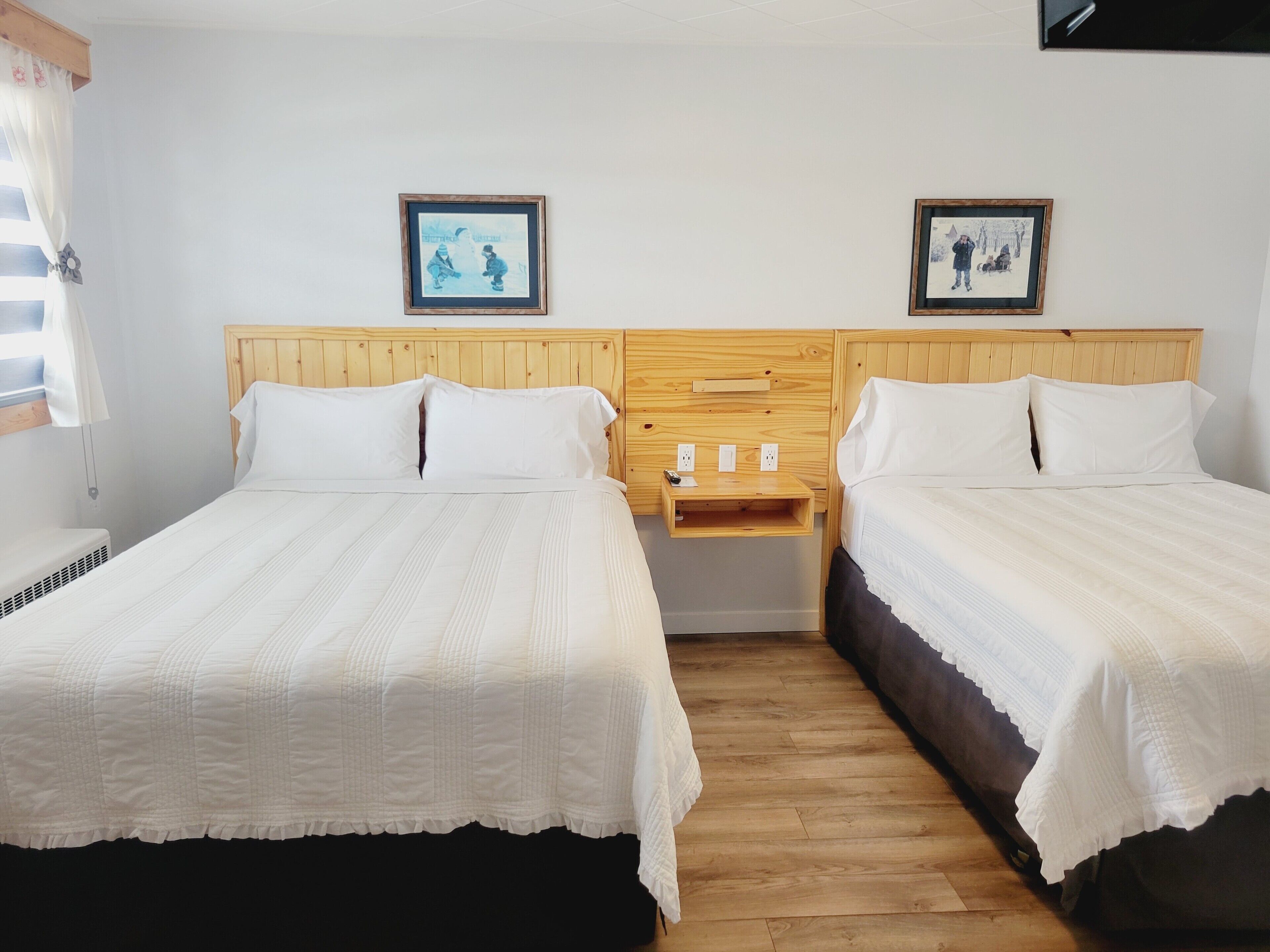 Una habitación con dos camas, cabeceros de madera, ropa de cama blanca y dos cuadros en la pared.