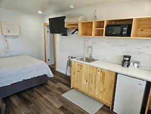 Una habitación pequeña con cama, una kitchenette compacta con microondas, cafetera y lavamanos.