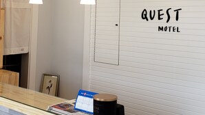 A motel interior with a reception desk, pendant lights, a calendar, and a wall sign reading 'QUEST MOTEL'. - Quest Motel (Whitewood)