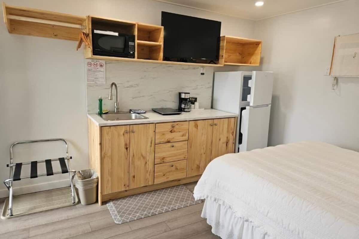 Quarto compacto com cama, cozinha compacta equipada com micro-ondas, geladeira e armários de madeira.