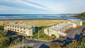 A coastal hotel with multiple buildings, a parking lot, and a beach view.