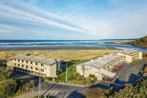 A coastal hotel with multiple buildings, a parking lot, and a beach view.