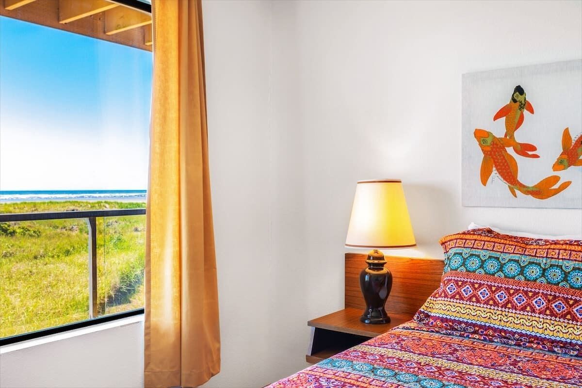 A hotel room with a bed, a nightstand with a lamp, a window with a view of the landscape, and a wall with a fish painting.