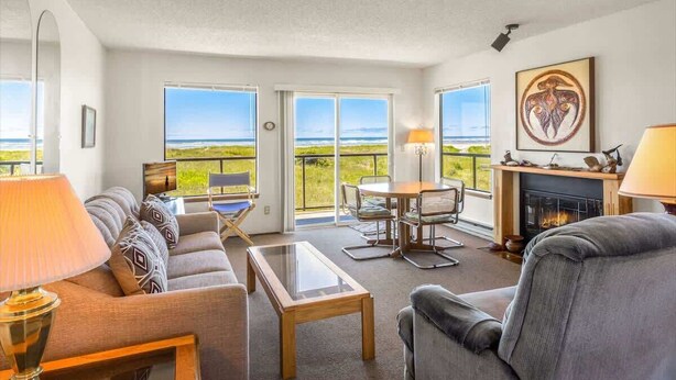 A living room with a sofa, a coffee table, a fireplace, and a view of the ocean.