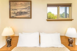 Habitación de hotel con cama, dos mesitas de noche, un cuadro, una ventana y una lámpara en cada mesita.