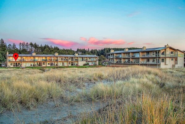 Un hotel con varias edificaciones, un área verde al frente y un bosque en el fondo.