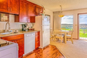 A kitchen with wooden cabinets, a refrigerator, a dishwasher, and a dining area with a table and chairs.