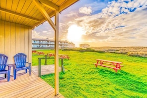 A covered outdoor area with picnic tables and chairs, a grassy field, and buildings in the background.