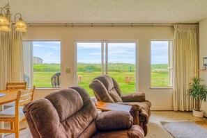 A living room with a large window, a dining table, and two recliner chairs.