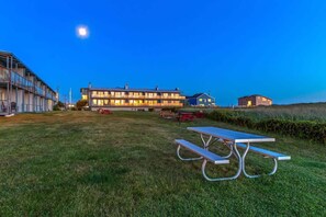 A grassy area with a picnic table, a building with multiple windows, and a moon in the sky.