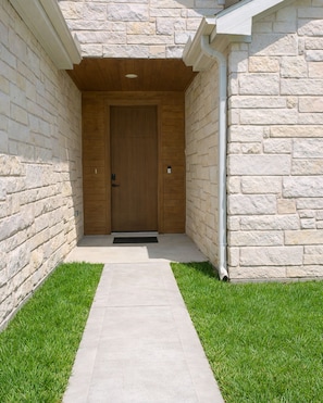 Ein Steinhaus mit einer Holztür und einem Betonweg, der davorführt.