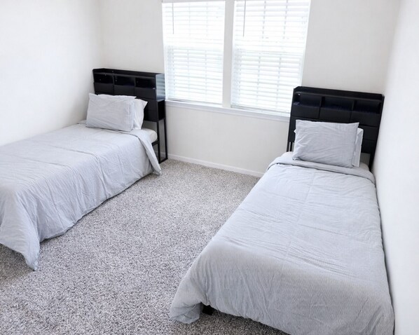 A bedroom with two single beds, a window with blinds, and a carpeted floor.