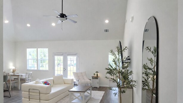 A spacious living room with a white sofa, a coffee table, a white armchair, a dining area with a table and chairs, and a large mirror. - Spacious private home in Cleveland, TX. Sleeps 6-8. Huge backyard for gatherings (Cleveland)