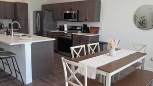 A modern kitchen with a central island, stainless steel appliances, and a dining area with white chairs and a wooden table. - Spacious private home in Cleveland, TX. Sleeps 6-8. Huge backyard for gatherings (Cleveland)