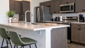 A modern kitchen with a central island, stainless steel appliances, and bar stools. - Spacious private home in Cleveland, TX. Sleeps 6-8. Huge backyard for gatherings (Cleveland)