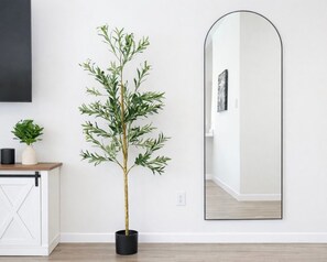 Une pièce avec une plante en pot, un miroir et un meuble blanc.